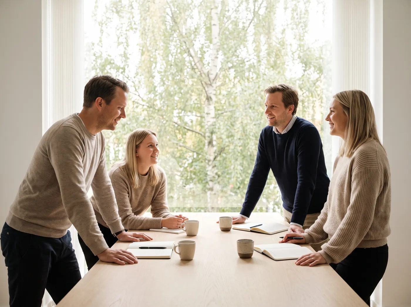 Fyra medarbetare står runt ett mötesbord med anteckningsblock och kaffekoppar under en genomgång
